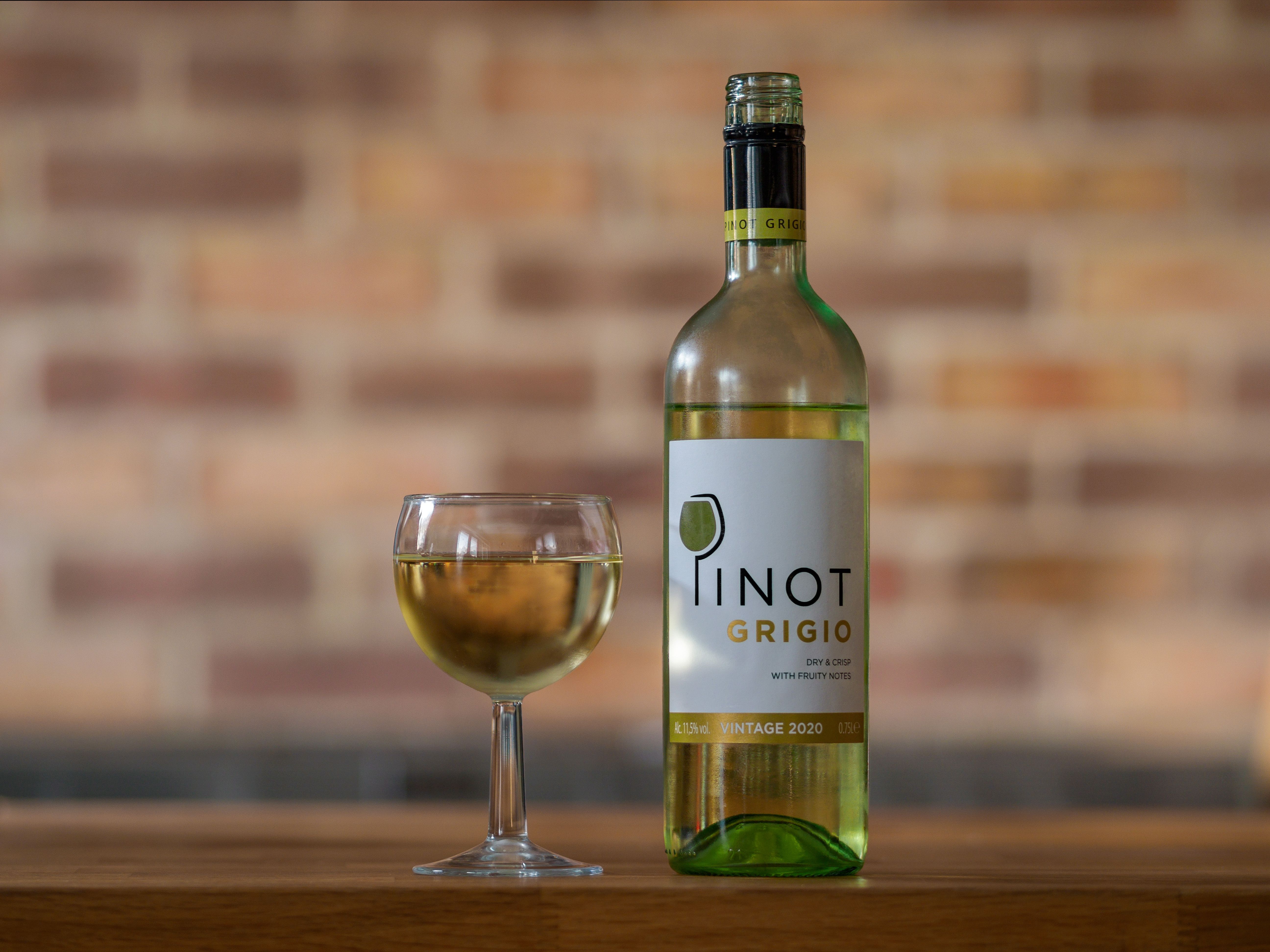 Fles pinot grigio naast een vol glas witte wijn tegen een bakstenen muur