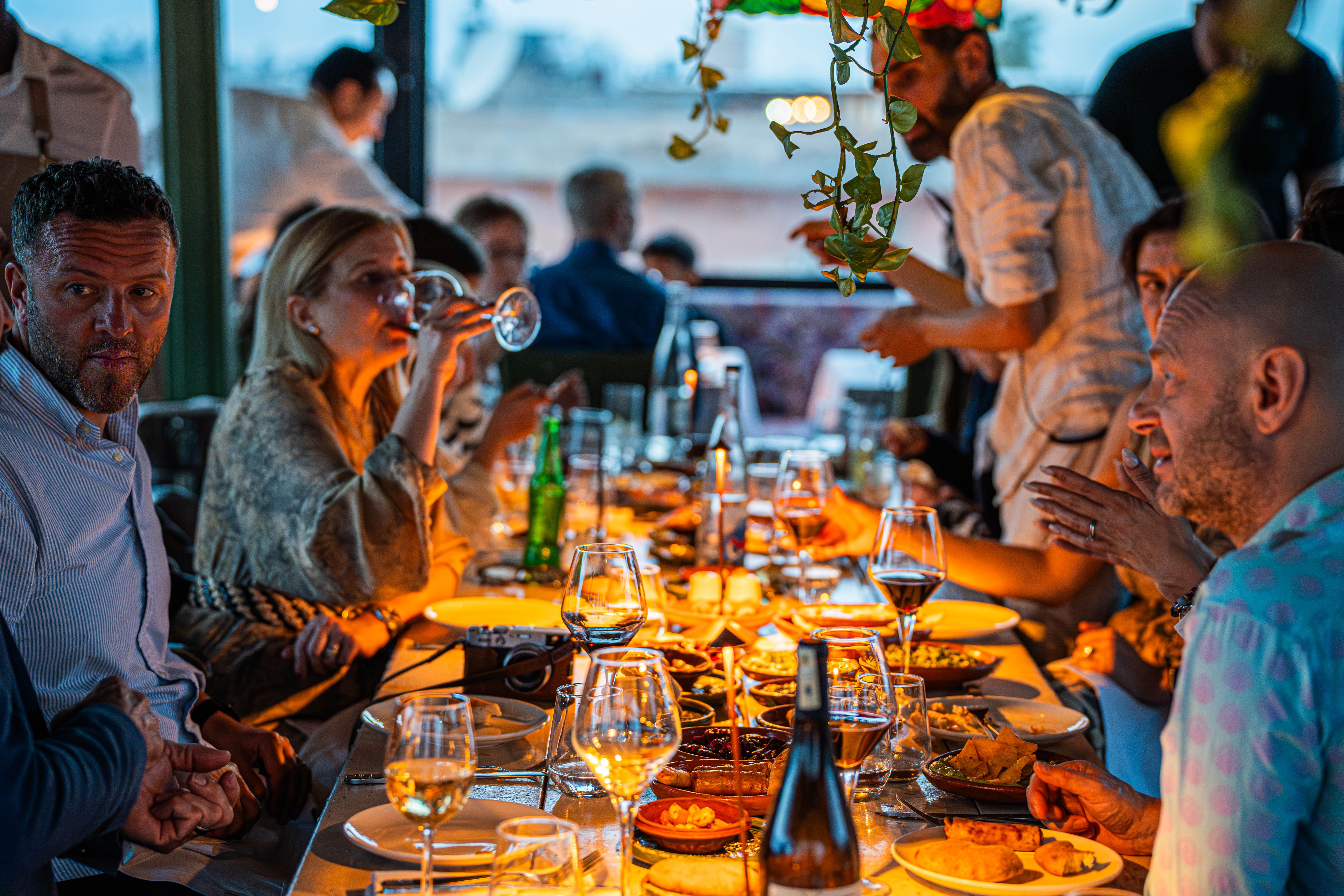 Lange terrastafel vol gerechten en wijnglazen tijdens een diner in gouden avondlicht